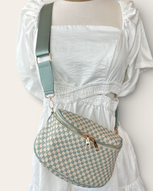 Front view of the Light Blue Checkered Saddle Crossbody Bag worn over a white dress, featuring a vegan leather woven design and wide adjustable strap.