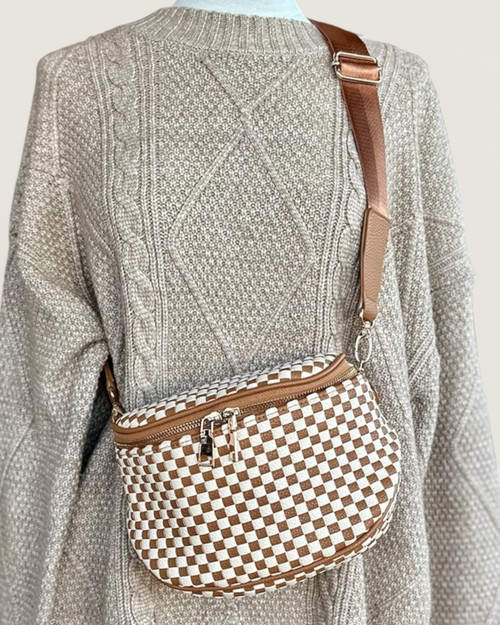 Front view of the Tan Checkered Saddle Crossbody Bag worn over a grey sweater, featuring a woven vegan leather design and adjustable brown strap.