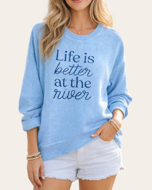 Front view of a woman wearing the light blue Better At The River corded sweatshirt, styled with white denim cut-off shorts.