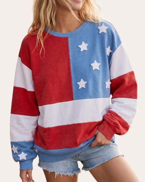 Front view of a woman modeling a cozy red, white, and blue Americana flag pullover sweatshirt with distressed star patches.