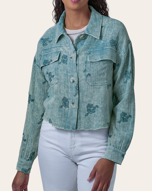 Front view of a woman wearing the button-down washed emerald double gauze jacket with floral embroidery over white pants.