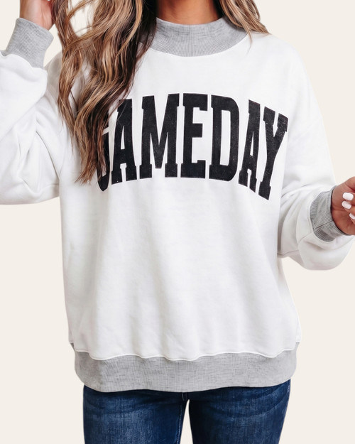Woman wearing the heather white side of a reversible mock neck sweatshirt with black GAMEDAY graphics