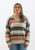 Front view of a woman in a relaxed-fit, multicolored striped sweater from Trendy Threads Boutique's Spring collection. The sweater features a combination of soft pastel and earth tones in horizontal stripes, with a V-neckline and ribbed cuffs and hem. She is wearing light blue denim jeans and has straight, shoulder-length hair. The background is a simple, clean white, emphasizing the sweater's colors.