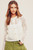 A confident woman models a chic white open-knit cardigan with a delicate daisy pattern, paired with olive green high-waisted shorts, creating a sophisticated and comfortable spring outfit.