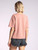 A rear view of the woman in the rose tee, displaying the back of the tee's relaxed fit and the frayed hem of her black shorts, emphasizing the laid-back style.