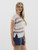 Side view of a woman wearing the "Tell Me Everything Top," showcasing the striped pattern and ribbed hem detail, paired with denim shorts.