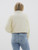 Back view of the Jayda Jacket, featuring a cream puffer design and cozy knit sleeves, paired with light wash jeans for a fall-ready outfit.