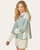Angled view of a woman wearing a sage striped hooded top with ivory waffle sleeves and drawstring detail, styled with cream button-front shorts.