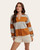 Front view of a woman wearing a rust and grey horizontal striped pullover top with long sleeves and a collar, styled with cream shorts