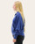 Side profile of a woman modeling a blue quarter-zip pullover sweatshirt with front pockets.