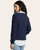 Back view of woman wearing a navy ribbed V-neck sweater over a light chambray shirt with light-wash jeans.