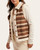 Side view of the relaxed fit patterned sherpa vest layered over a cream long-sleeve top.