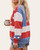 Woman wearing an oversized Americana flag sweatshirt holding a mug, side view showing red and white stripes with blue and white star details on the sleeve.