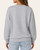 Back view of a woman modeling a light grey crewneck pullover sweatshirt perfect for fall weather.