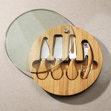 A round bamboo cheese board set featuring four stainless steel knives and a corkscrew, with a glass lid.