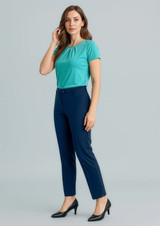 A woman stands wearing a teal top and navy slim leg pants, paired with black high heels. The pants feature a logo.