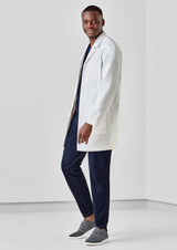 A male model wearing a white longline lab coat over navy pants and grey sneakers, posing in a neutral setting.