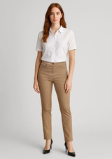 A woman stands wearing slim leg stretch chino pants in tan and a white collared shirt, paired with heels.