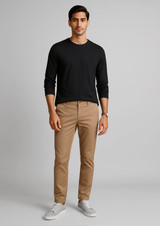 A man is wearing tan tapered stretch chino pants paired with a black long-sleeve shirt and white sneakers.
