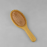 A bamboo hair brush with a rounded shape and wooden bristles on a natural wood base.