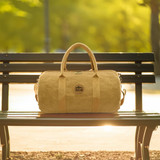 A kraft paper duffle bag in a tan colour sits on a park bench, featuring handles and a logo.