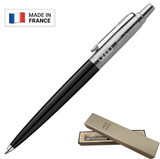 A black ballpoint pen sits in a beige box, featuring a silver clip and branding on the side.