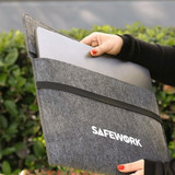 A grey felt laptop sleeve is being held, with a laptop partially inserted. It has a logo on the front. A grey felt laptop sleeve is being held, with a laptop partially inserted. It has a logo on the front.