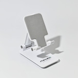 A white folding desktop mobile phone and tablet stand with a textured grey surface. It features a logo on the base.