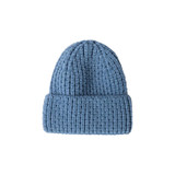 A blue twisted cable cuffed beanie with a ribbed texture and a fold at the bottom. It features a logo on the side.
