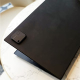 A black laptop on a marble table, featuring a small black SwiftFinder Smart Tag Tracker attached to the corner.