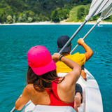A pink cap is worn by a person kayaking in blue waters, with a backdrop of greenery and hills.