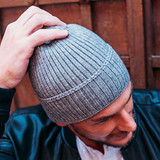 A grey ribbed beanie worn by a person. The beanie has a fitted design and a subtle logo on it.