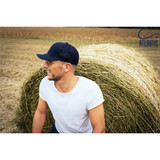 A navy cap resting on a man with short hair and glasses, sitting near a straw bale in a rural setting.