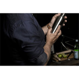 A close-up of a man holding a metal cocktail shaker, wearing a navy blue patterned button-up shirt.