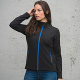 A black women's softshell jacket with blue zip accents and two side pockets, displayed on a model against a concrete background.