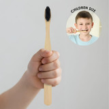 A bamboo toothbrush in a child's hand, featuring a black bristle head and a natural wood handle.