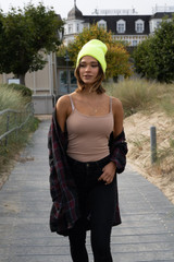 A luminescent safety acrylic beanie in neon yellow, worn by a person with a light top and a plaid shirt, walking outdoors.