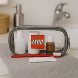 A grey clear travel case containing a toothbrush, toiletry bottles, and a tube, with a logo visible on the front.