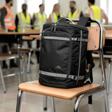 A black High Sierra travel backpack sits on a chair in a classroom, with people in high-visibility vests in the background.
