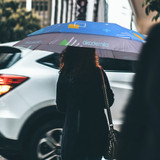 An expandable golf umbrella in shades of blue, held by a person, featuring a logo and geometric designs.