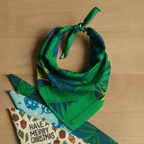A green bandana featuring a tropical leaf design, tied in a knot on a wooden surface.