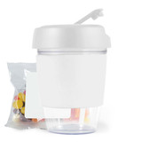 A white reusable coffee cup with a lid, accompanied by a bag of colorful jelly beans.