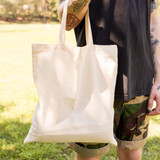 A short handle tote bag in a natural canvas color is held by a person, featuring a simple and minimalist design.