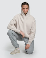 A unisex premium fleece oversized hoodie in light grey, worn by a model with grey tracksuit bottoms and sneakers.