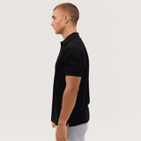 A black polo shirt displayed on a male model, showing a side profile view. The shirt features a logo.