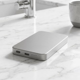 A silver power bank with a sleek design, featuring USB ports, resting on a marble surface.