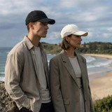 A black cap and a white cap worn by a man and a woman against a coastal backdrop. The caps have logos.