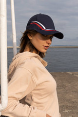 A navy cap with curved embroidery in red and white, worn by a woman near a waterfront.