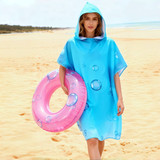 A blue double-sided fleece hooded change towel with bubbles design, worn by a person holding a pink inflatable ring on the beach.