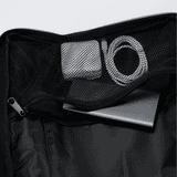 A black Eiger backpack interior featuring a metal device, tape, and a charging cable inside a mesh pocket.